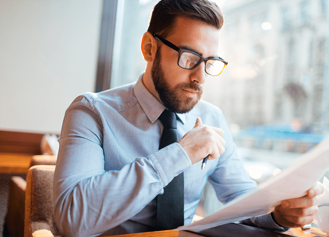 A man wearing glasses and a tie is looking at a piece of paper in a commercial or industrial setting.