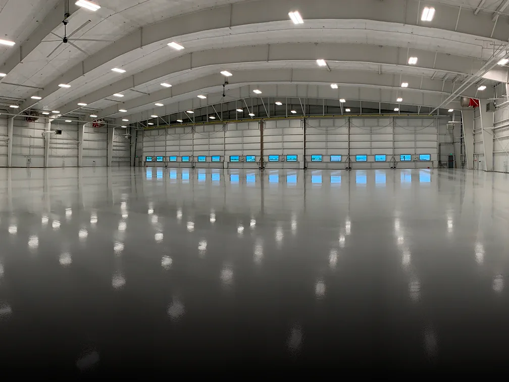 A vast hangar with an aviation flooring and bright lights.