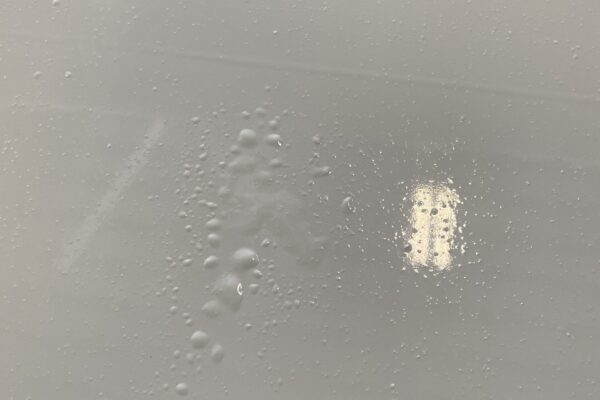 A smooth, light gray surface with scattered water droplets and a bright rectangular light reflection near the center right.