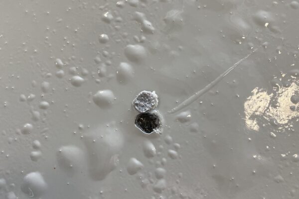 Close-up of a light gray, glossy surface with two small, round holes near the center and scattered raised bumps around them.