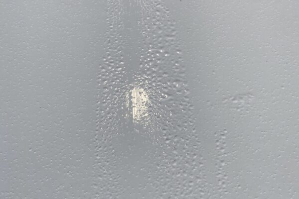 Close-up of a light gray painted surface with numerous small bubbles and imperfections, and a black vent or grate at the top edge of the image.