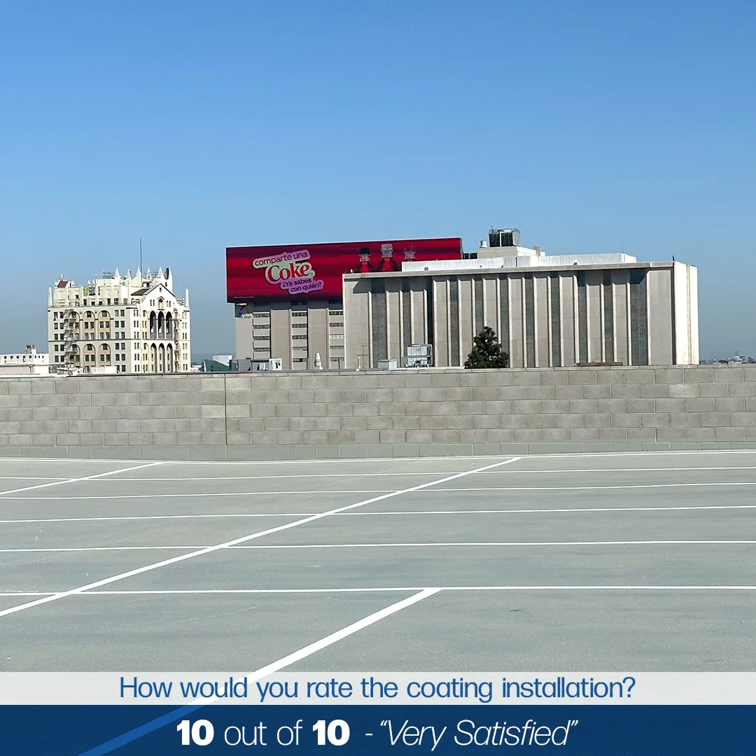 A rooftop parking lot with a tall concrete wall, buildings in the background, and a large Coca-Cola billboard under a clear blue sky. Text at the bottom reads "10 out of 10 - 'Very Satisfied'".