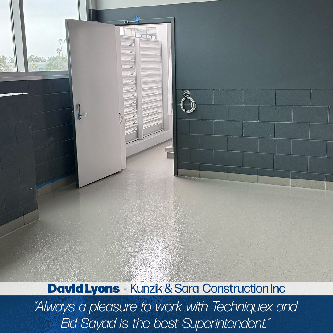 A clean, empty room with gray walls and a shiny light gray floor, an open door, a window with shutters, and a metal ring mounted on the wall.