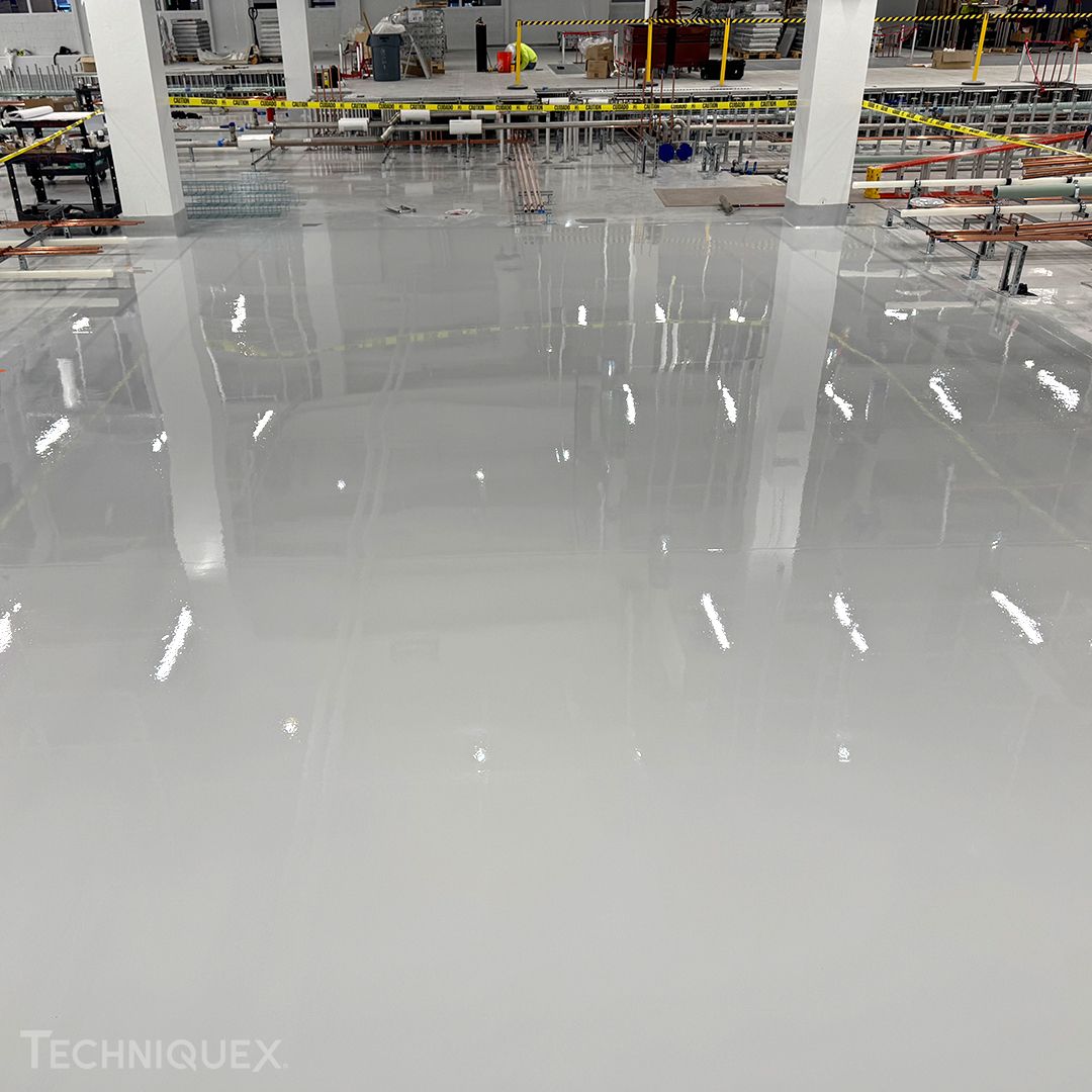 A large, freshly coated epoxy floor in an industrial facility displays a reflective surface and construction materials in the background, illustrating the differences between resin flooring vs epoxy flooring in such environments.