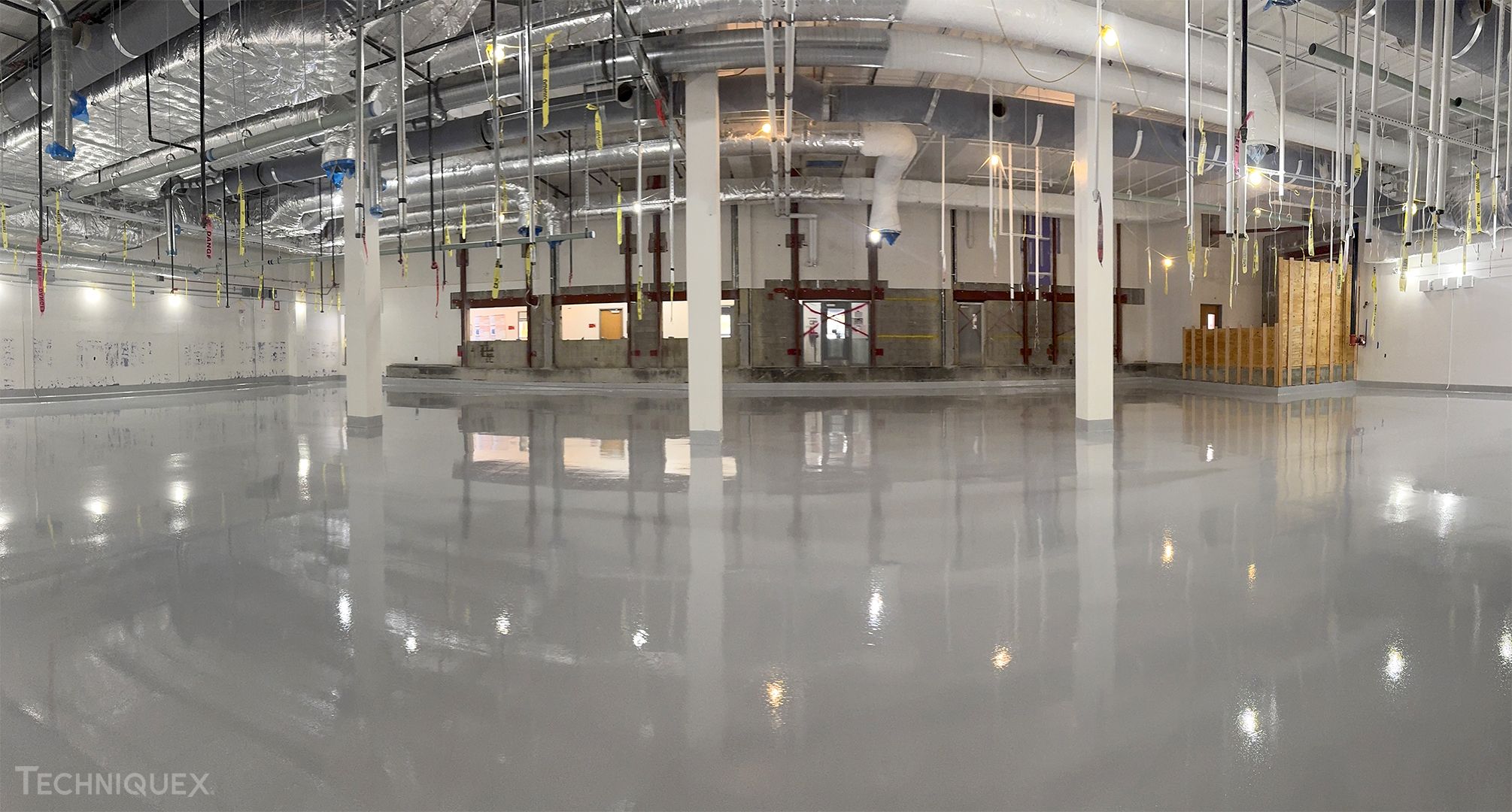 Interior of a large industrial building under construction, featuring exposed pipes, ductwork, and a highly polished concrete floor—perfect for comparing Resin Flooring vs Epoxy Flooring solutions.