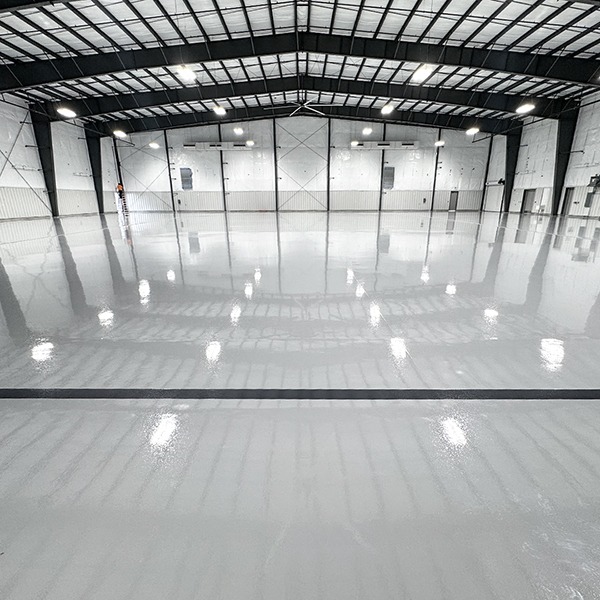 Large, empty industrial warehouse with a glossy, polished concrete floor and high ceiling with exposed beams and lights.