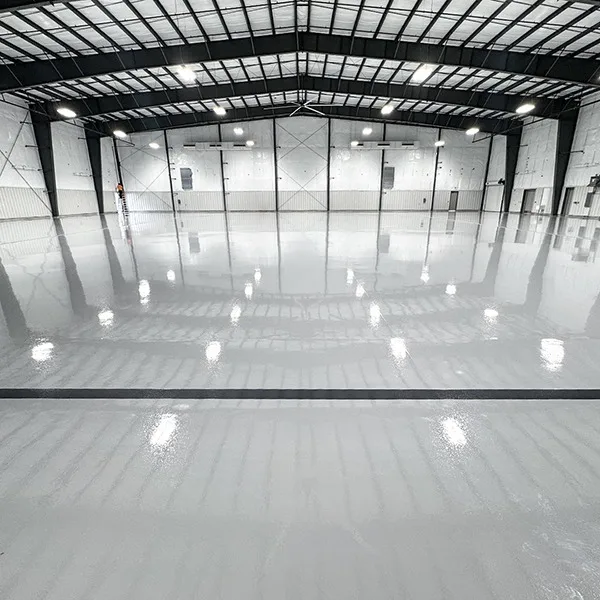Large, empty industrial warehouse with a glossy, polished concrete floor and high ceiling with exposed beams and lights.