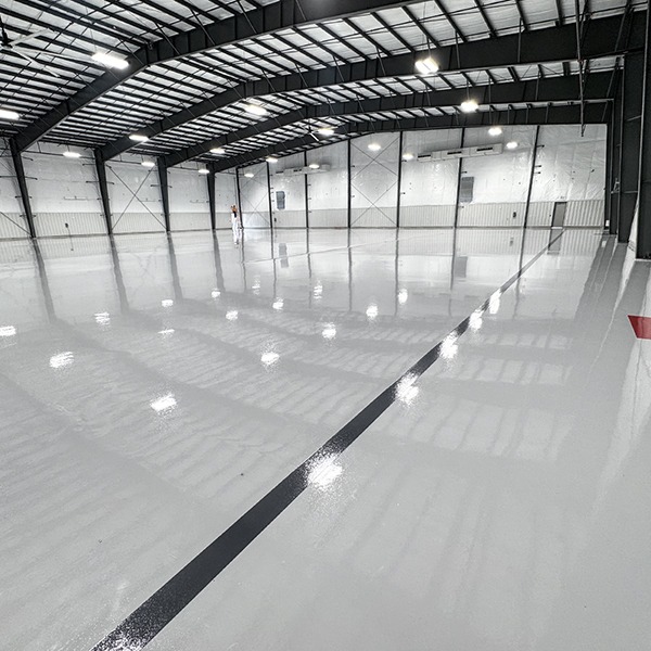 Large indoor facility with a glossy, reflective floor and high ceilings, lit by overhead lights. A single black line runs across the floor, and one person is visible in the distance.