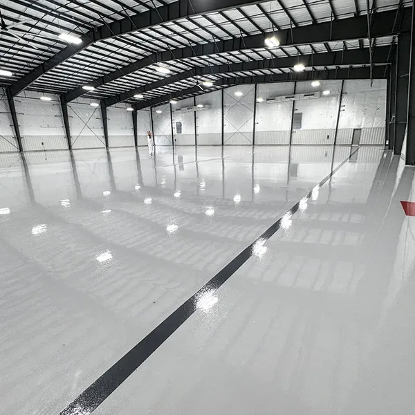 Large indoor facility with a glossy, reflective floor and high ceilings, lit by overhead lights. A single black line runs across the floor, and one person is visible in the distance.