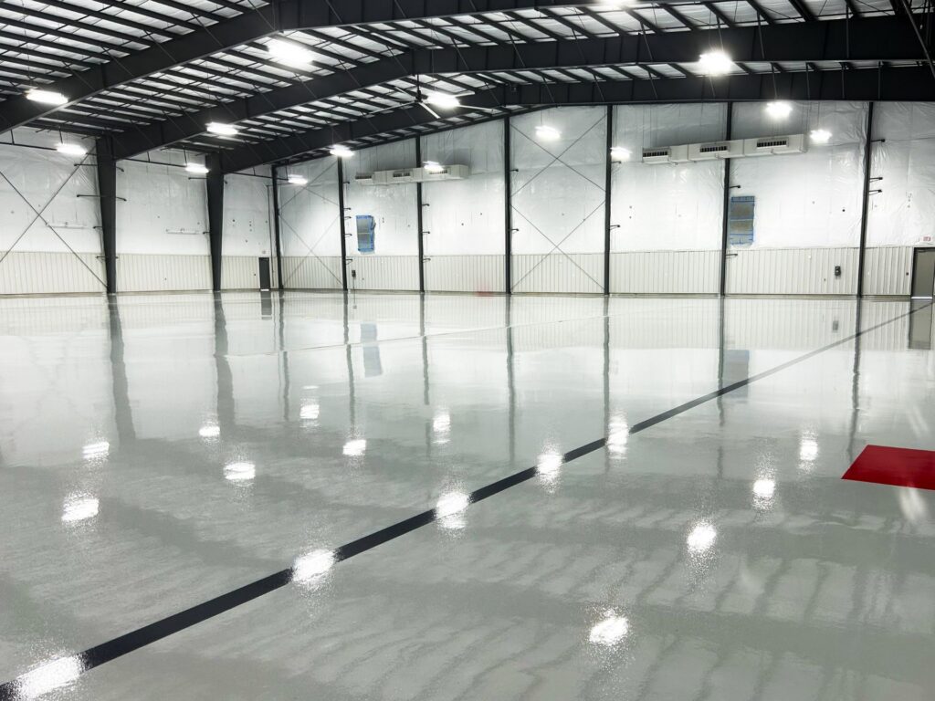 Large, empty indoor facility with a shiny polished concrete floor, metal beams, and white insulated walls; a black line and red rectangle are marked on the floor.