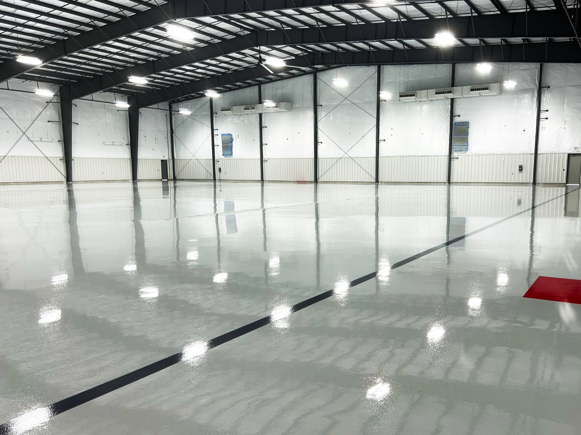 Large, empty indoor facility with a shiny polished concrete floor, metal beams, and white insulated walls; a black line and red rectangle are marked on the floor.