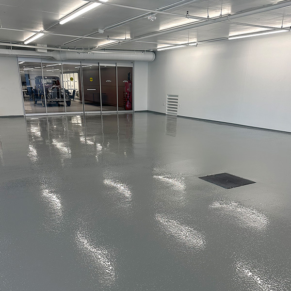 A large, empty room with a shiny, gray epoxy-coated floor and glass doors leading to another area in the background.