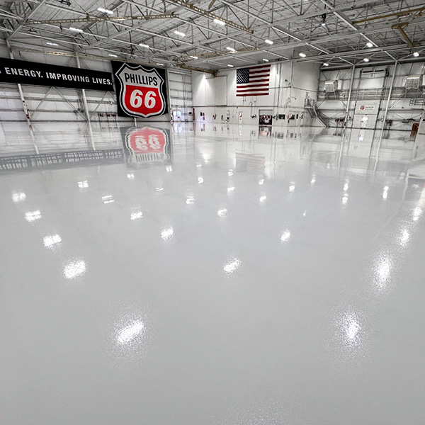 A large, empty aircraft hangar with a polished floor, an American flag on the back wall, and a Phillips 66 sign displayed to the left.