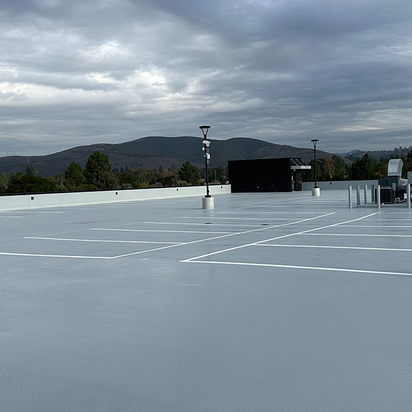 Empty rooftop parking lot with freshly painted white lines under a cloudy sky, surrounded by trees and hills in the background.