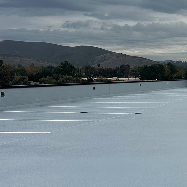 Empty rooftop parking lot with painted parking lines, bordered by trees and hills under a cloudy sky.