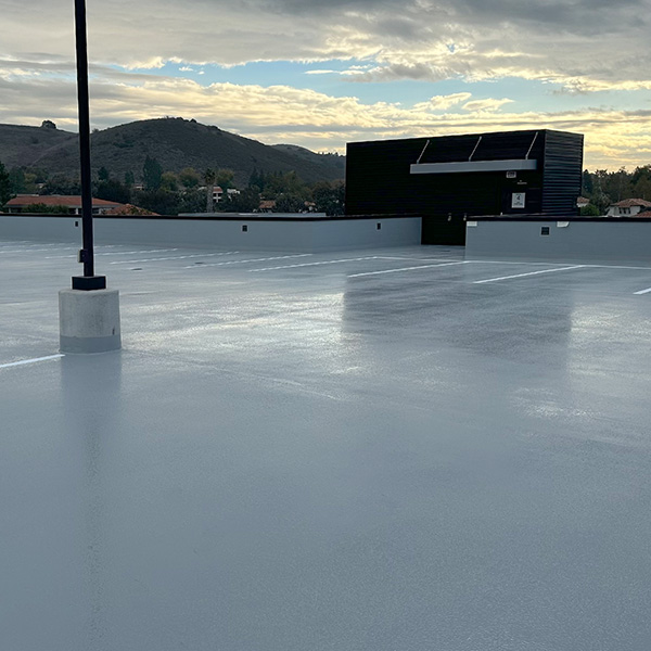 Empty rooftop parking lot with a light pole, a small black building, and distant hills under a cloudy sky.