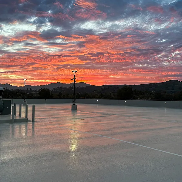 Empty parking lot at sunset with dramatic orange and purple clouds in the sky, distant mountains visible on the horizon.