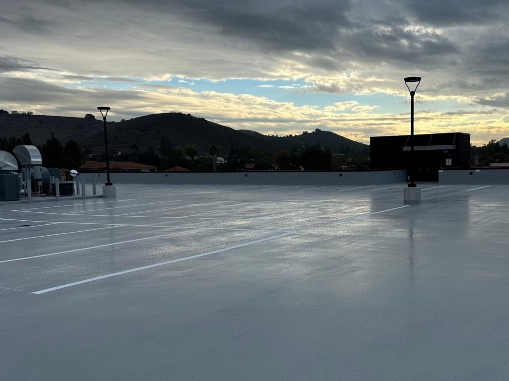 A nearly empty rooftop parking lot at dusk with distant hills and a cloudy sky in the background.