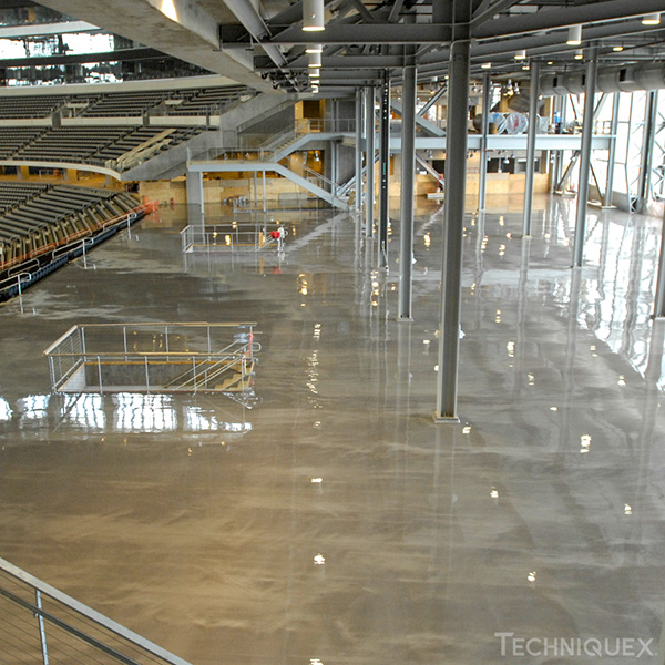 Large indoor stadium area with rows of seating on the left and a smooth, reflective concrete floor. Exposed beams and columns are visible throughout the space.