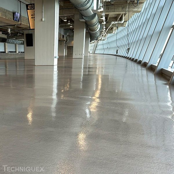 A large, empty indoor space with a shiny, polished concrete floor, exposed ceiling pipes, and slanted windows along one side.