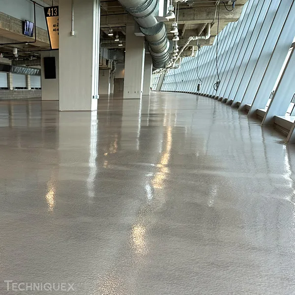 A large, empty indoor space with a shiny, polished concrete floor, exposed ceiling pipes, and slanted windows along one side.