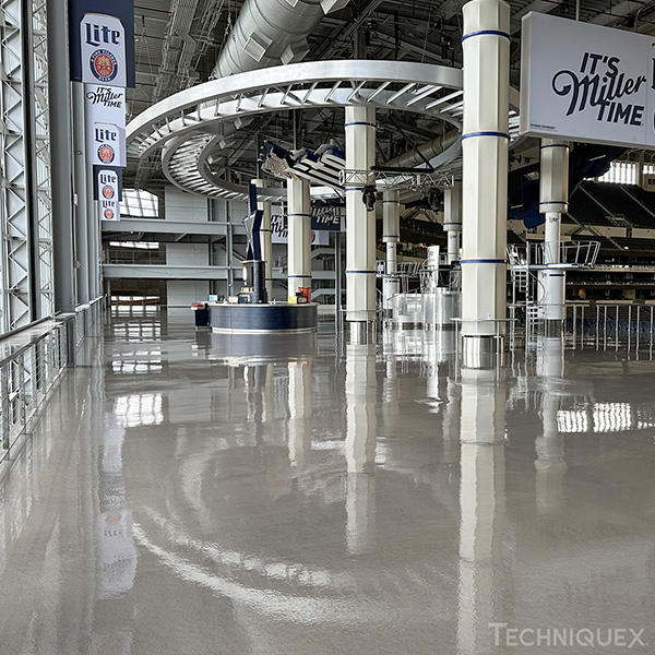 A large indoor stadium concourse with polished concrete floors, a circular overhead structure, and signage advertising Miller Lite.