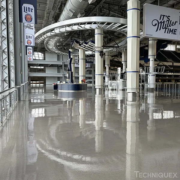 A large indoor stadium concourse with polished concrete floors, a circular overhead structure, and signage advertising Miller Lite.