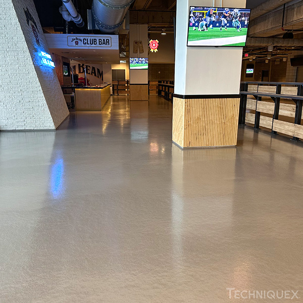 A polished concrete floor in a sports bar area with TVs showing a football game and signs for Club Bar and Team.