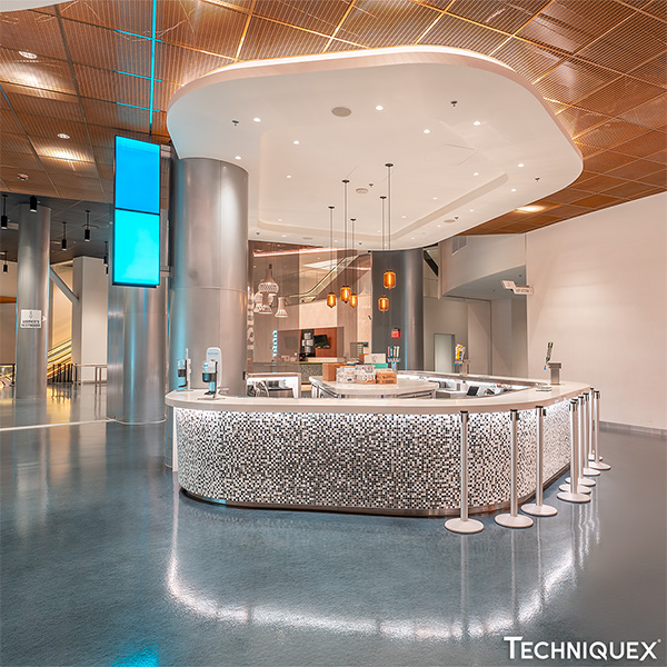 A modern café counter with mosaic tile design, surrounded by stanchions, is set in a spacious lobby with glossy floors, high ceilings, and contemporary lighting.