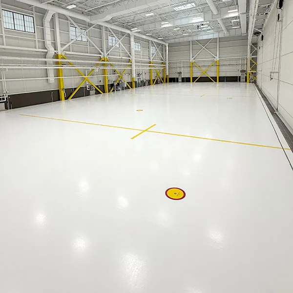 Large, empty industrial warehouse with white floors, yellow line markings, high ceilings, and exposed beams.