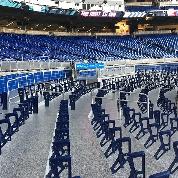 Rows of empty blue folding chairs are arranged in curved lines inside a large, empty stadium with blue seats in the background.
