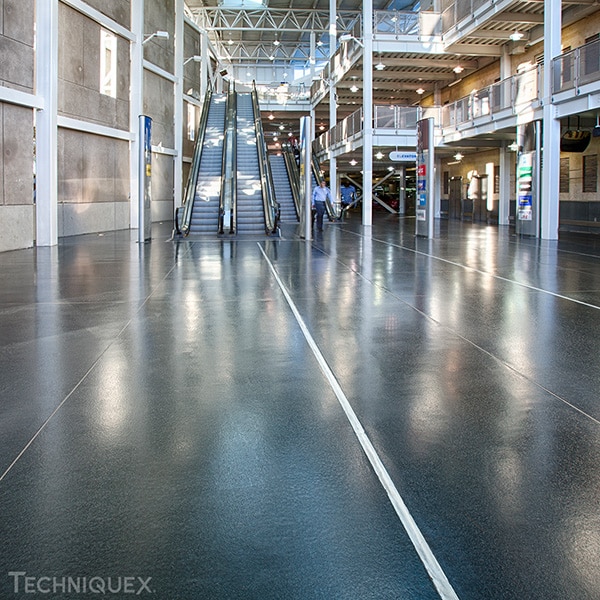 Interior of a modern building with shiny polished floors, escalators in the center, high ceilings, and people walking in the background.