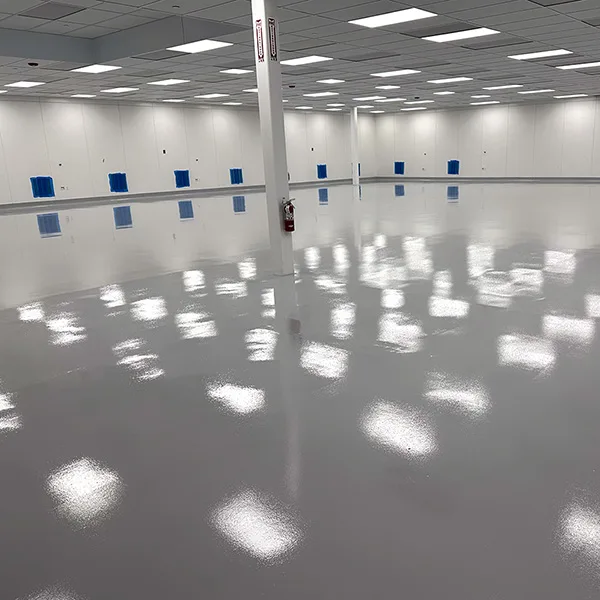 Large empty room with glossy, reflective flooring, white walls, a grid ceiling with bright lights, and a fire extinguisher mounted on a column.