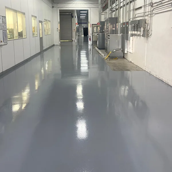 A clean, shiny gray floor in an industrial hallway with electrical panels and windows on the left wall.