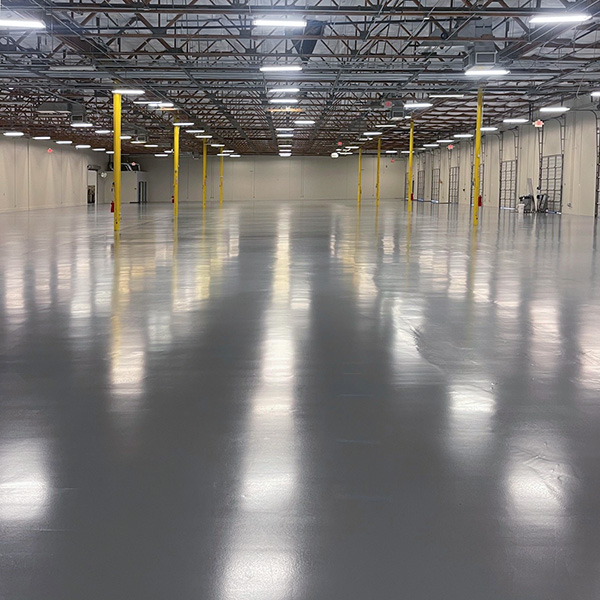 Large, empty warehouse interior with polished concrete floor, yellow support columns, high ceiling, and industrial lighting.