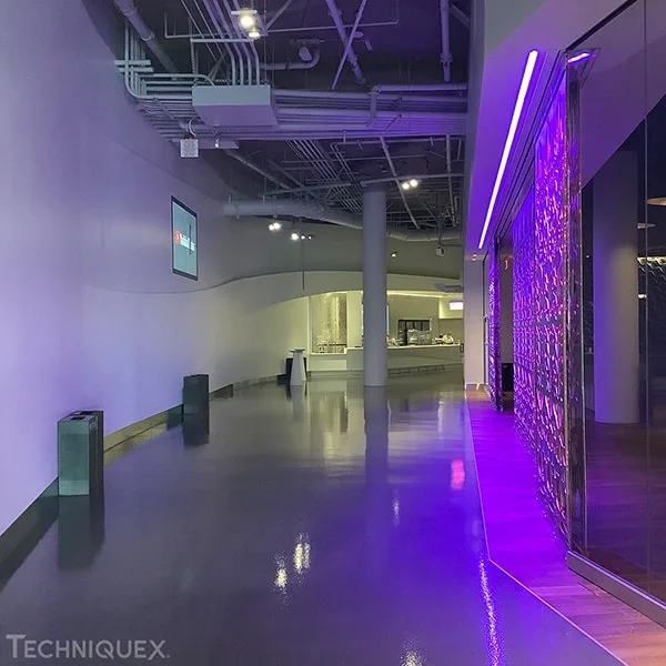 A modern, curved hallway with shiny floors, a wall-mounted screen on the left, and purple accent lighting on the right near a glass partition.