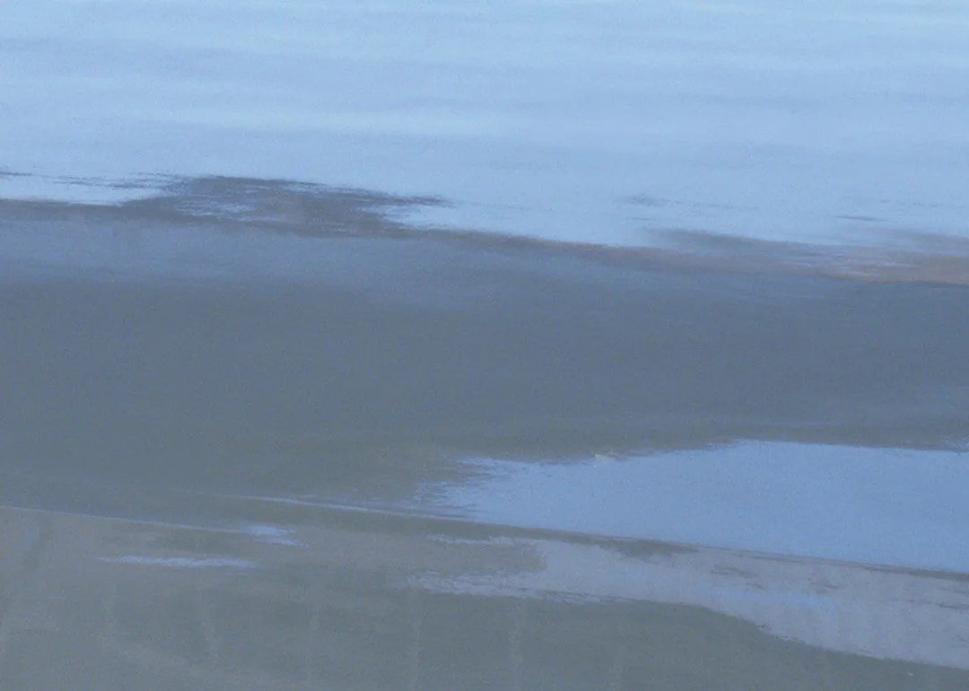 Calm ocean water with a gentle wave approaching the shore, reflecting the blue sky above—a scene as clear and serene as understanding the difference between polyaspartic vs epoxy.
