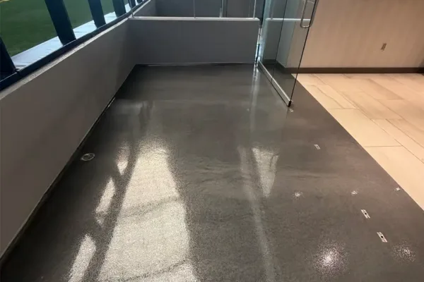 A sleek, private stadium suite balcony with polished gray flooring, overlooking an empty football field.