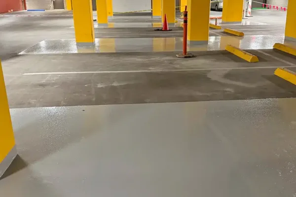 Underground parking garage with gray epoxy floors and bright yellow support pillars.