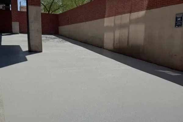 A grey, speckled concrete surface leading toward a brick wall and a concrete pillar.