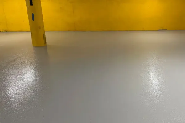 An empty parking garage with a yellow wall, a pillar marked with the number 1, and an Exit sign with an arrow pointing left.