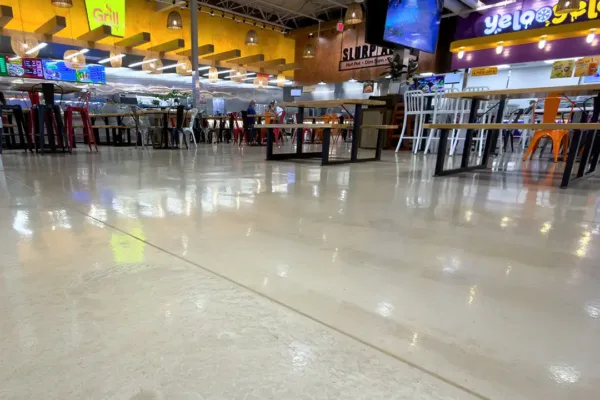 View from floor level of a food court featuring multiple vendor stalls, including “Grill” and “Yelo,” with tables, chairs, and hanging pendant lights.