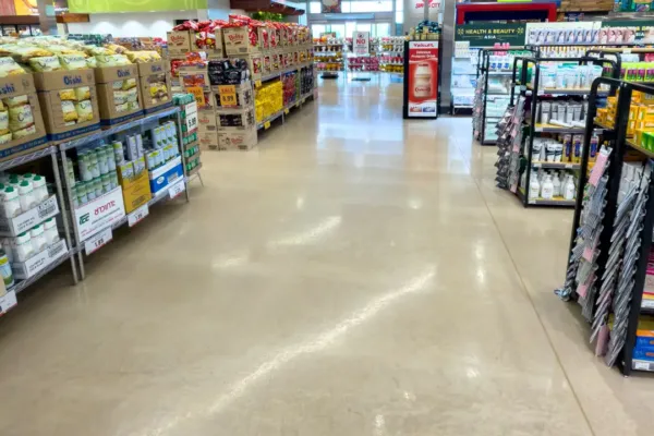 Aisle view of a grocery store with shelves stocked with snacks, beverages, and health products, including signage for “cut fruit” and “Grill City.”