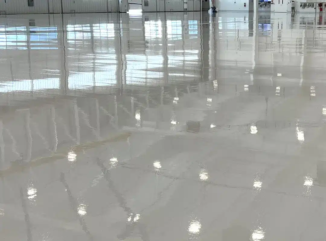 A wide, empty industrial warehouse with a high-gloss, reflective white floor showcasing the aesthetic finish of polyaspartic vs epoxy.